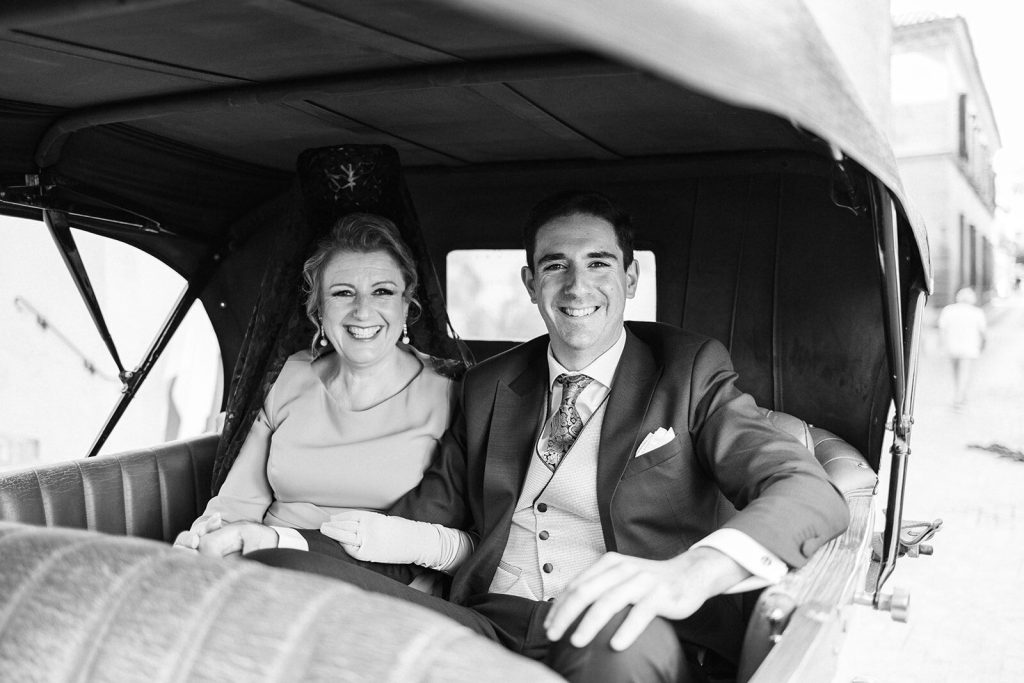 Los novios sonriendo en el interior de un coche de época
