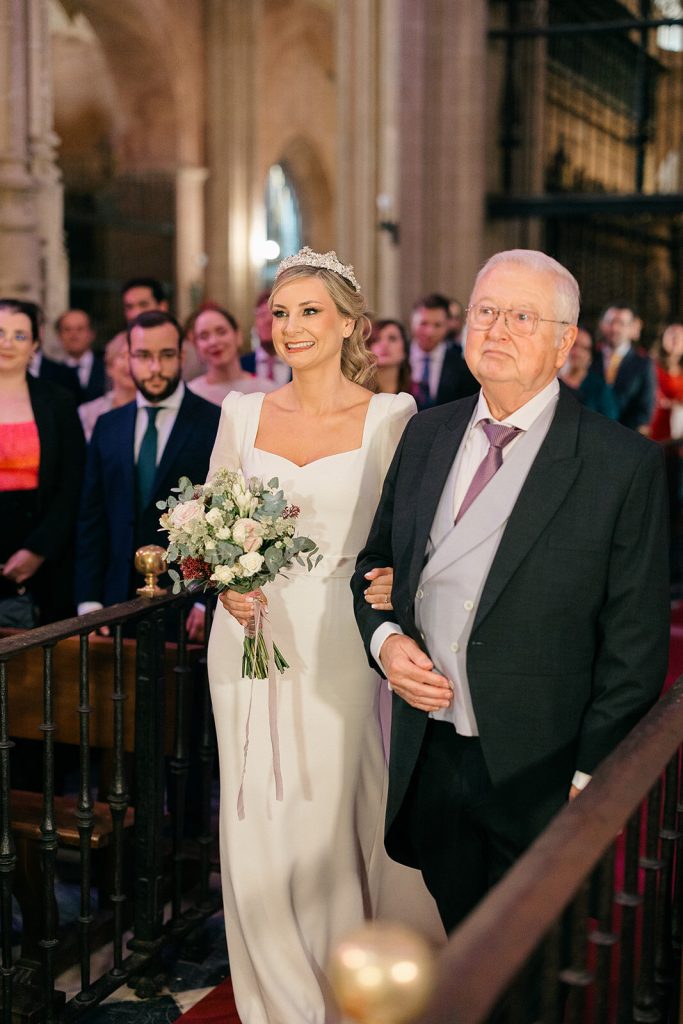 Entrada de la novia y su padre en la ceremonia, con los invitados en pie